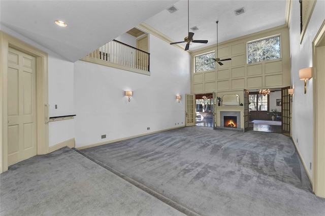 unfurnished living room with carpet floors, a wealth of natural light, a warm lit fireplace, and visible vents