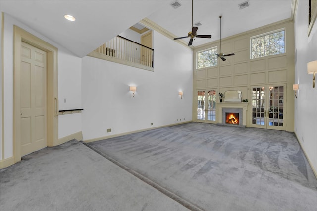 unfurnished living room featuring a warm lit fireplace, a high ceiling, visible vents, and carpet flooring