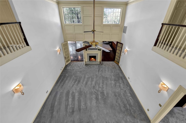 living area featuring visible vents, a ceiling fan, carpet flooring, a lit fireplace, and baseboards