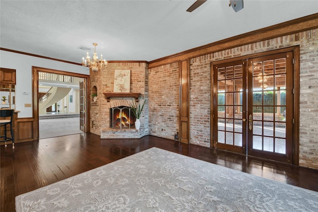 unfurnished living room with visible vents, brick wall, hardwood / wood-style floors, a textured ceiling, and french doors