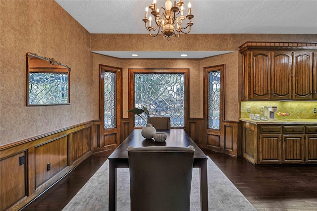 dining space with an inviting chandelier, dark wood finished floors, a textured ceiling, and wainscoting