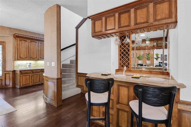 bar with stairs, dark wood-type flooring, a wainscoted wall, and wet bar