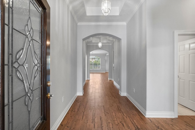 corridor featuring baseboards, crown molding, arched walkways, and hardwood / wood-style floors