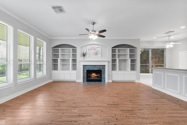 unfurnished living room featuring built in shelves, visible vents, light wood-style floors, and crown molding