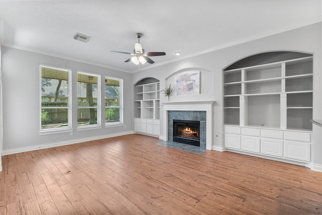 unfurnished living room with light wood finished floors, baseboards, visible vents, built in features, and crown molding