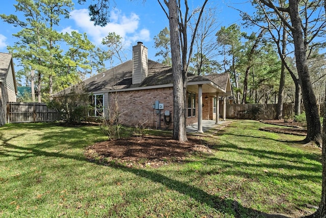 view of side of property featuring a yard, brick siding, a chimney, and a fenced backyard