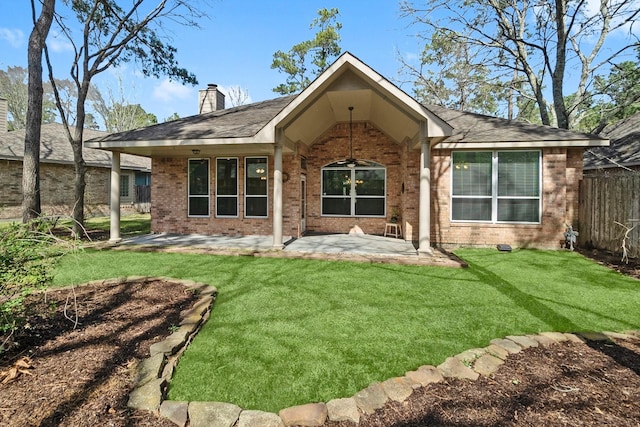 rear view of house featuring brick siding, a patio, a chimney, and a lawn