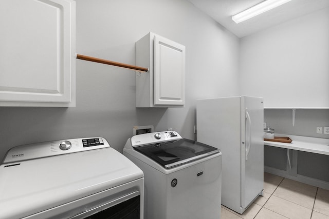 clothes washing area featuring cabinet space, light tile patterned floors, and washing machine and clothes dryer