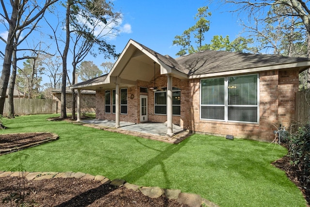 back of house with brick siding, a shingled roof, fence, a yard, and a patio area