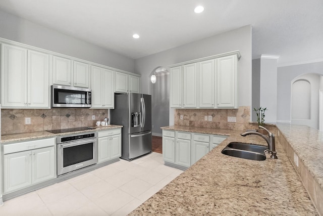 kitchen with arched walkways, tasteful backsplash, appliances with stainless steel finishes, white cabinets, and a sink