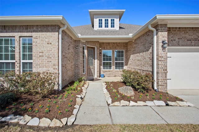 view of exterior entry featuring an attached garage, a shingled roof, and brick siding