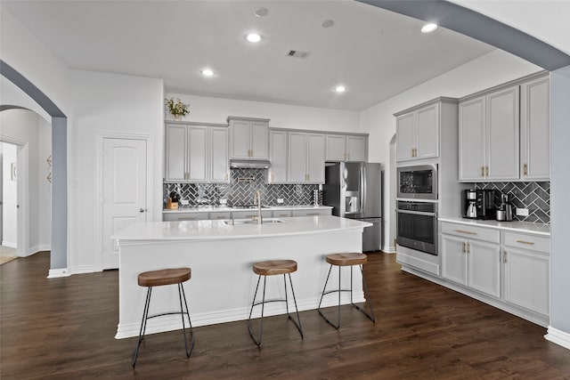 kitchen featuring visible vents, arched walkways, appliances with stainless steel finishes, a breakfast bar area, and gray cabinets