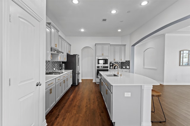 kitchen featuring arched walkways, gray cabinets, appliances with stainless steel finishes, a sink, and a kitchen breakfast bar