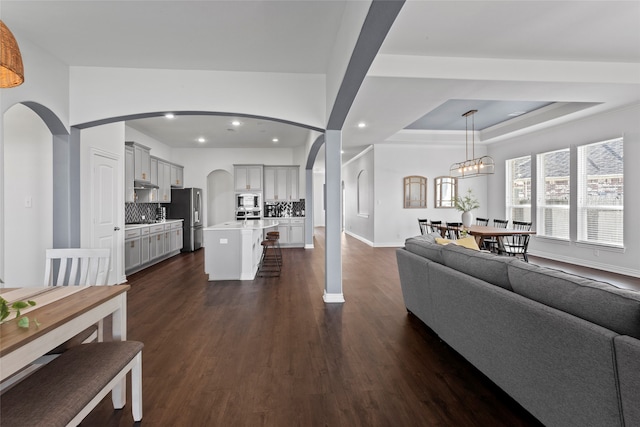 living area featuring dark wood-type flooring, a tray ceiling, arched walkways, and recessed lighting