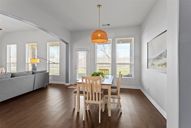 dining area with arched walkways, visible vents, dark wood finished floors, and baseboards