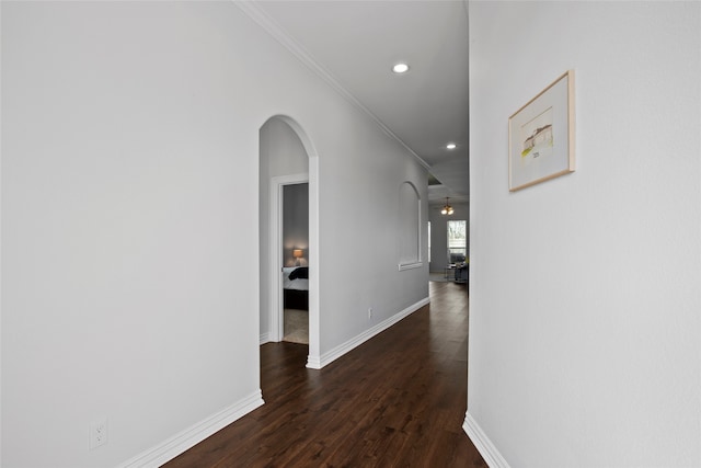 hall featuring arched walkways, baseboards, dark wood-style floors, and crown molding