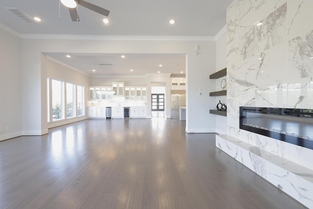 unfurnished living room with beverage cooler, a premium fireplace, visible vents, and dark wood-type flooring