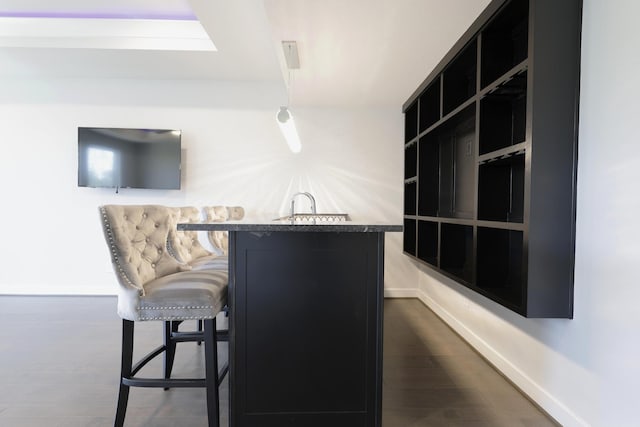 bar featuring dark wood-type flooring, wet bar, and baseboards