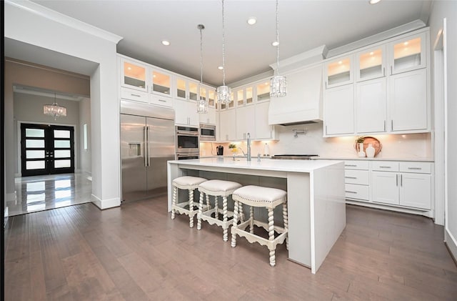 35 Papado Trails Cir, The Woodlands, TX 77375 - kitchen featuring built in appliances, light countertops, a center island with sink, white cabinets, and a kitchen breakfast bar