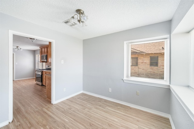 empty room with visible vents, light wood-style floors, a healthy amount of sunlight, a textured ceiling, and baseboards