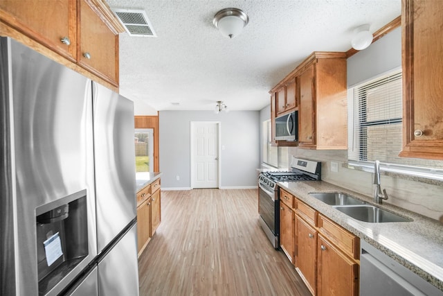 kitchen with light wood finished floors, visible vents, appliances with stainless steel finishes, brown cabinetry, and a sink