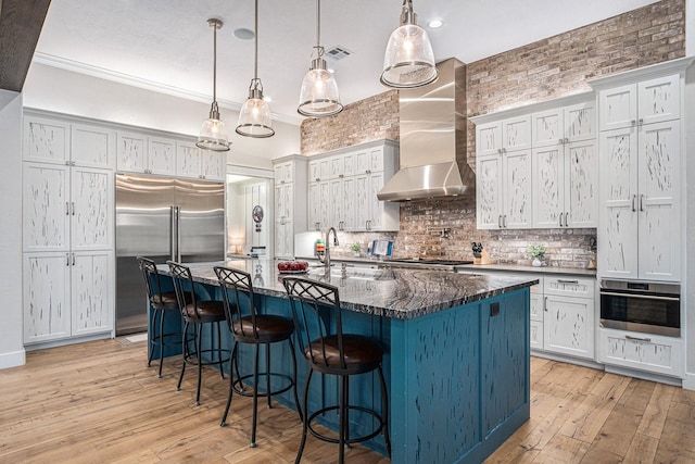 kitchen with a breakfast bar, a sink, appliances with stainless steel finishes, wall chimney exhaust hood, and tasteful backsplash