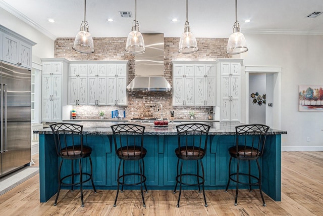 kitchen featuring wall chimney exhaust hood, visible vents, crown molding, and built in refrigerator