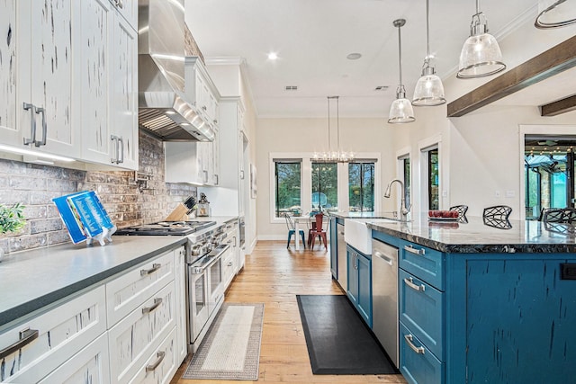 kitchen with wall chimney exhaust hood, appliances with stainless steel finishes, ornamental molding, blue cabinets, and a sink