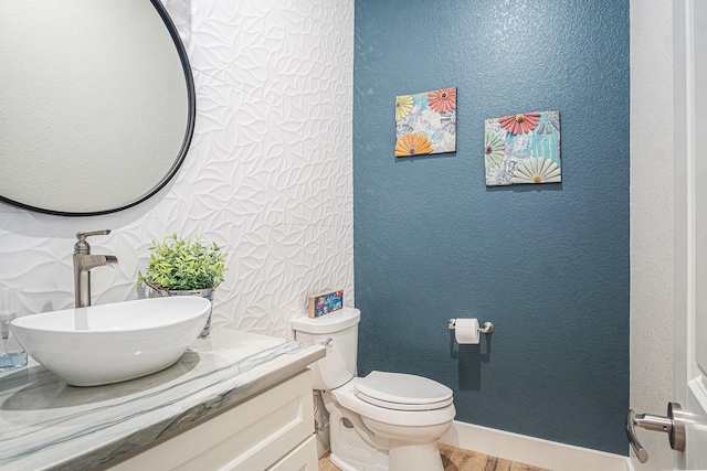 half bathroom with a textured wall, vanity, toilet, and wood finished floors