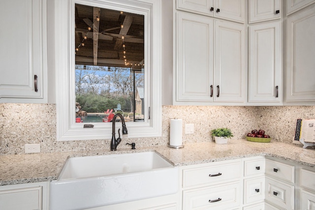 kitchen featuring light stone counters, backsplash, a sink, and white cabinetry