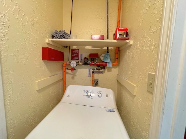 clothes washing area with washer / clothes dryer, laundry area, and a textured wall