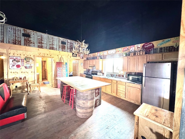 kitchen with a towering ceiling, appliances with stainless steel finishes, wood finished floors, a center island, and light countertops