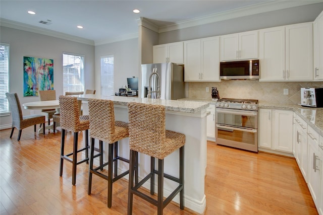 kitchen with light wood-style flooring, an island with sink, ornamental molding, stainless steel appliances, and tasteful backsplash