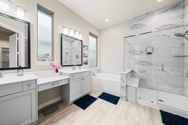 bathroom with a garden tub, a sink, wood finished floors, two vanities, and a stall shower