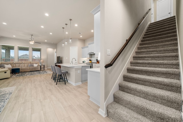 interior space featuring a breakfast bar, open floor plan, a kitchen island with sink, light countertops, and light wood-style floors