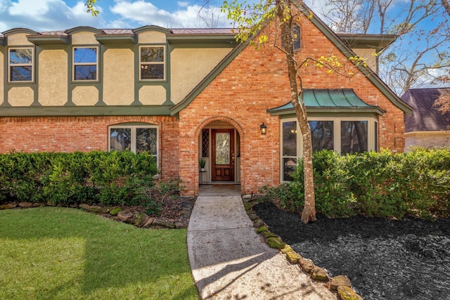 view of front of home with a front yard, brick siding, and stucco siding