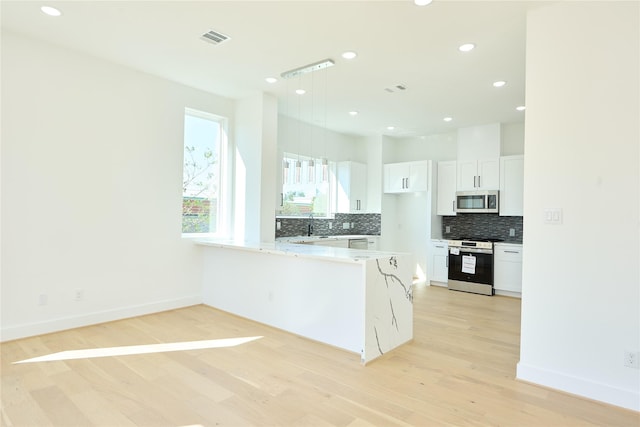 kitchen with visible vents, appliances with stainless steel finishes, a peninsula, white cabinetry, and backsplash