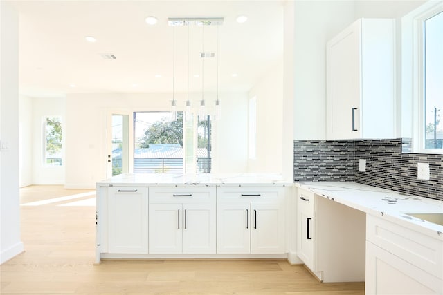 kitchen with white cabinets, a peninsula, light stone countertops, light wood-style floors, and backsplash