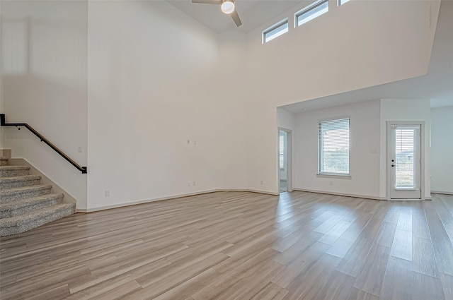 unfurnished living room with light wood-style flooring, stairway, ceiling fan, and baseboards