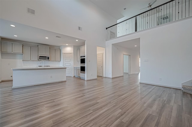 unfurnished living room featuring light wood-type flooring, a sink, visible vents, and baseboards