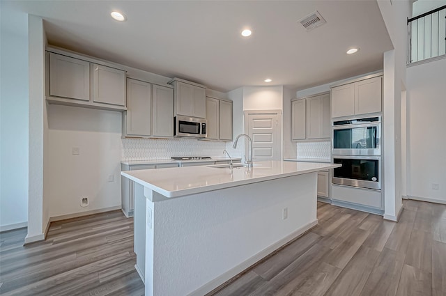 kitchen with stainless steel appliances, tasteful backsplash, gray cabinets, visible vents, and light wood-style flooring