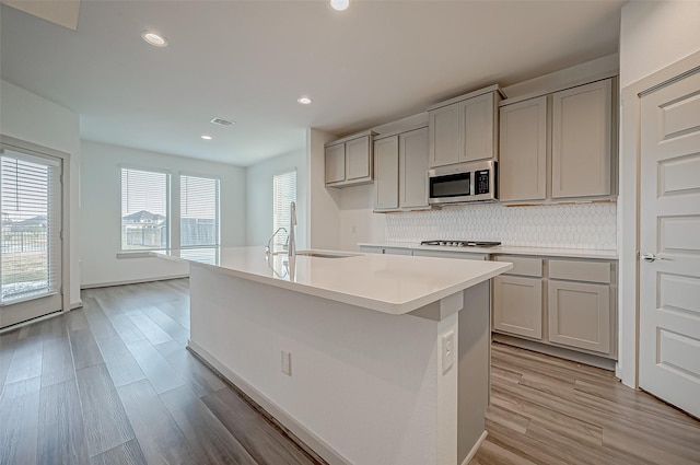 kitchen featuring gray cabinetry, stainless steel appliances, a sink, light wood-style floors, and backsplash