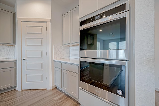 kitchen with tasteful backsplash, light countertops, light wood-style flooring, gray cabinetry, and double oven