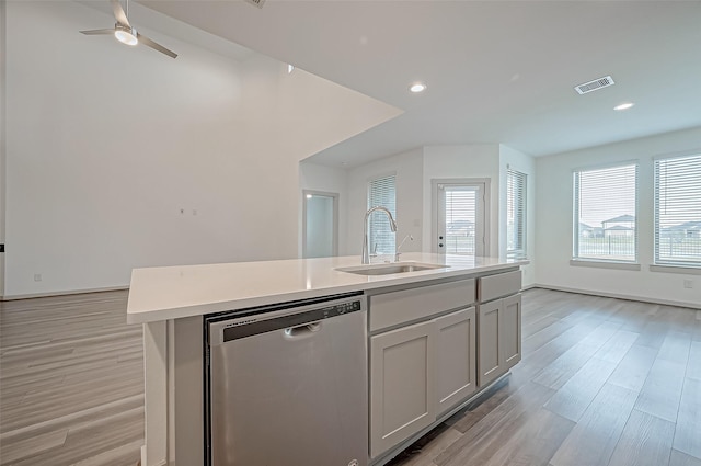 kitchen with light wood finished floors, visible vents, a kitchen island with sink, stainless steel dishwasher, and a sink