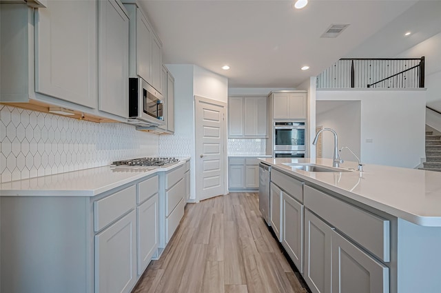 kitchen with gray cabinetry, stainless steel appliances, a sink, light wood-style floors, and light countertops