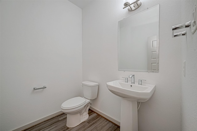 half bathroom with a sink, wood finished floors, toilet, and baseboards