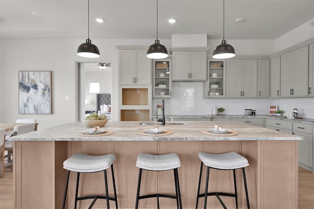 kitchen with tasteful backsplash, light wood-style floors, glass insert cabinets, a sink, and a kitchen breakfast bar