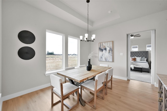 dining space featuring light wood-style floors, a raised ceiling, baseboards, and an inviting chandelier