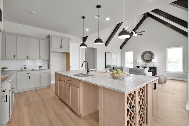 kitchen with a kitchen island with sink, a sink, light wood-style floors, open floor plan, and beamed ceiling