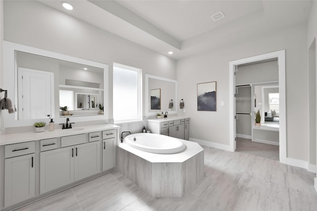 bathroom featuring a garden tub, two vanities, a sink, visible vents, and baseboards